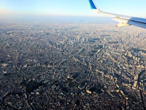 西日に照らされて立体感が強調される関東の都市風景を飛行機から眺める。